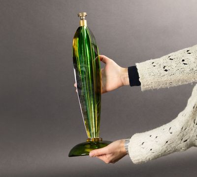 someone is holding a green glass vase in their hand on a gray background