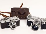 two cameras sitting next to each other on a white surface