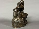 bronze statue of a man sitting on a rock with his hands on his knees