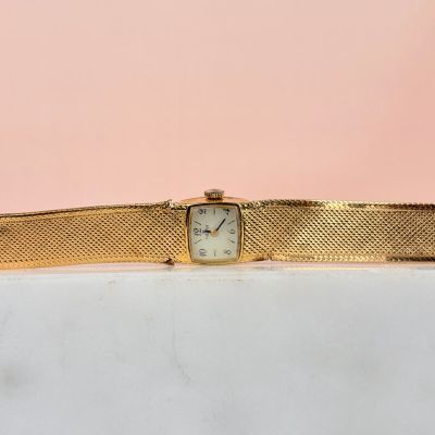 une montre-bracelet en or avec un cadran blanc sur fond rose