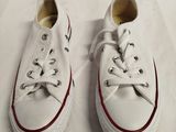 Des Converse blanches aux lacets rouges sont posées sur une surface blanche