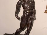 une statue en bronze représentant un homme en train de courir, posée sur un socle en marbre