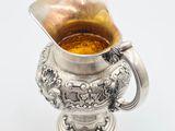 a silver vase with a liquid in it on a white surface