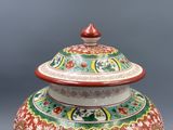 un vase rouge et vert muni d'un couvercle, posé sur une table