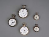 Plusieurs types de montres de poche sont exposés sur un support gris.