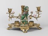 une figurine dorée et verte posée sur un socle orné de fleurs