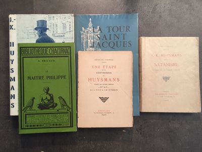 Plusieurs livres sont alignés sur une table, avec une horloge en arrière-plan.