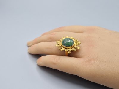 a close up of a person ' s hand wearing a gold ring with a green stone