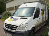 une camionnette blanche garée à côté d'un immeuble, avec une planche de surf sur le toit