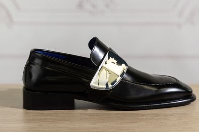 Le mocassin noir orné d'une boucle dorée est posé sur une table en bois.