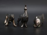 three silver figurines of animals sitting on a black surface