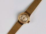 une image représentant une montre en or avec un cadran blanc posée sur une surface blanche