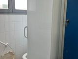 un réfrigérateur blanc dans une salle de bains, à côté d'une porte bleue