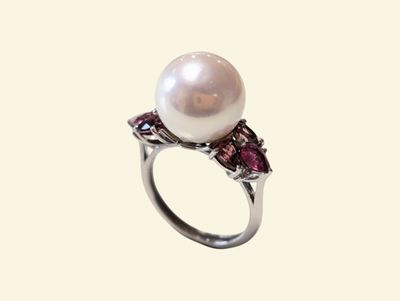 a close up of a ring with a pearl and garnets on it