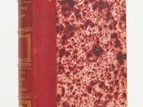 an old book with a red cover sitting on top of a white surface