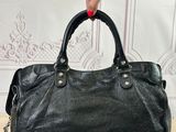 black leather handbag on a wooden table with a woman ' s hand holding it