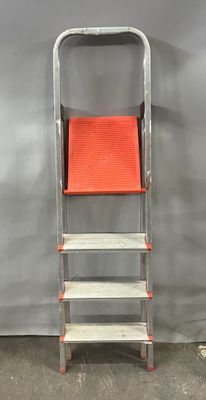 une photo représentant une échelle métallique avec un siège rouge, près d'un mur gris