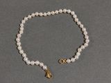 a close up of a white pearl bracelet with a gold clasp