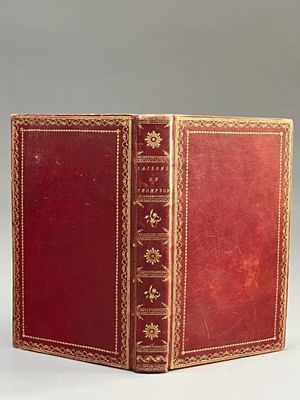 un vieux livre rouge aux tranches dorées posé sur une table blanche