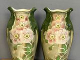 deux vases verts ornés de fleurs roses, posés sur une étagère en bois