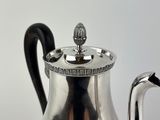 a silver tea pot with a black handle on a table