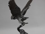 une statue en bronze représentant un oiseau perché sur une branche, les ailes déployées