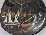 a black plate with a painting of boats on it