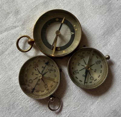 trois boussoles en laiton ancien posées sur un tissu blanc