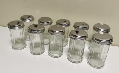 six glass jars with silver lids are lined up on a white surface