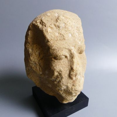 une sculpture en pierre représentant une tête, posée sur un socle noir