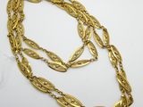 un collier en or composé d'une longue chaîne ornée d'un motif de feuilles