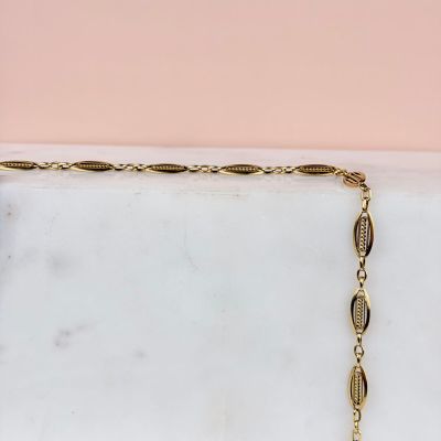 une photo d'un collier plaqué or posé sur une surface en marbre
