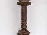 an antique wooden pedestal with a carved top on a white floor