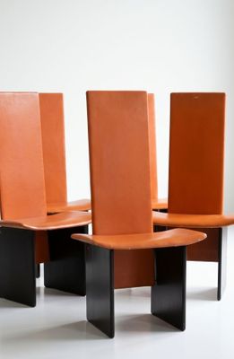 four chairs with orange leather seats sit in a row on a white surface