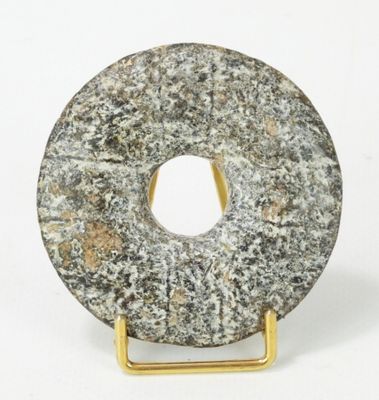 un beignet en pierre posé sur un socle doré, sur fond blanc