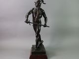 bronze statue of a man holding a sword and standing on a wooden base