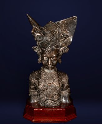une statue en argent représentant une femme à cornes, posée sur un socle en bois