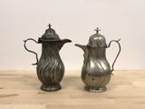 two silver coffee pots sitting on a wooden table
