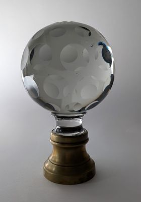 une boule de cristal posée sur un socle en bois, sur fond blanc