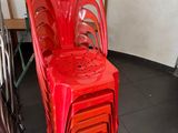 a red plastic chair sitting next to a stack of chairs