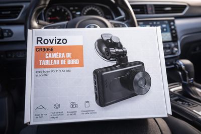 une personne tenant dans une voiture une boîte sur laquelle est fixée une caméra