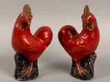 pair of red rooster figurines sitting on top of a tree stump