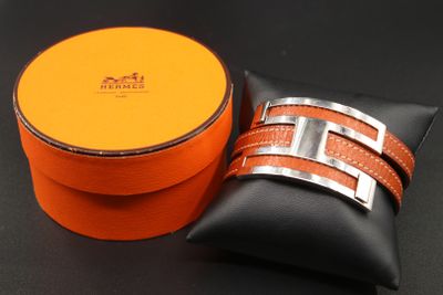 une boîte orange ornée d'une boucle argentée, posée à côté d'un oreiller noir