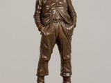 bronze statue of a man standing on a base with his hands in his pockets