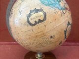 un petit globe sur un support en bois sur une surface rouge