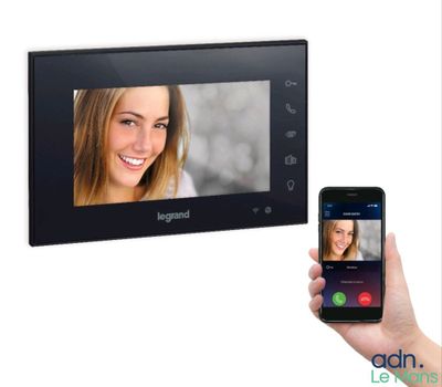 une personne tenant un smartphone devant un interphone vidéo