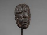 a wooden mask on a stand with a gray background