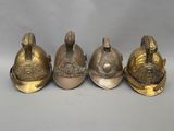 trois casques de pompier anciens en laiton, posés côte à côte sur une surface grise