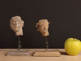 three sculptures of heads on a wooden stand next to an apple