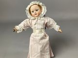 an old fashioned doll with a bonnet and dress is posed on a gray surface